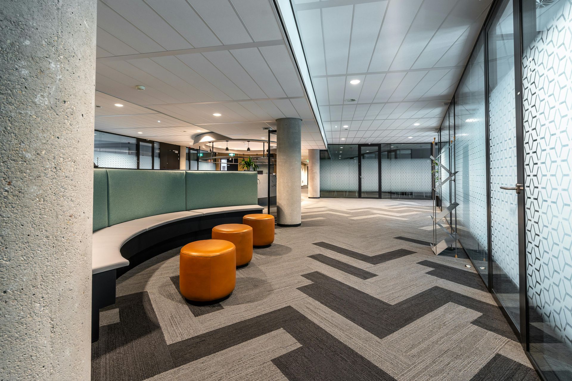A hallway with a chevron pattern on the floor and orange ottomans.