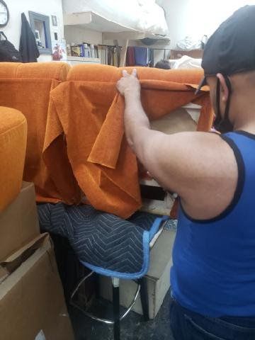 A man in a blue tank top is holding a piece of orange fabric.