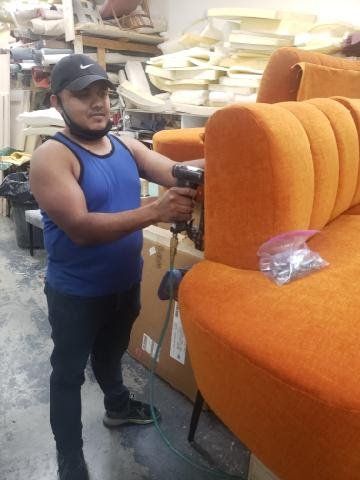 A man in a blue tank top is working on an orange couch