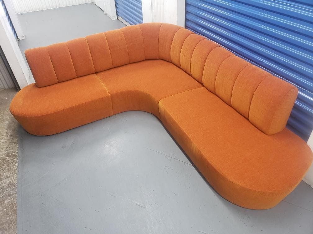 An orange sectional couch is sitting on a gray floor in a room.