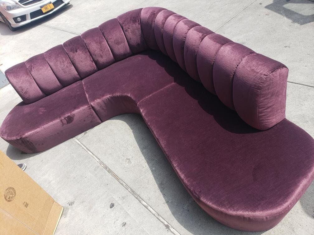 A purple sectional couch is sitting on the sidewalk next to a car