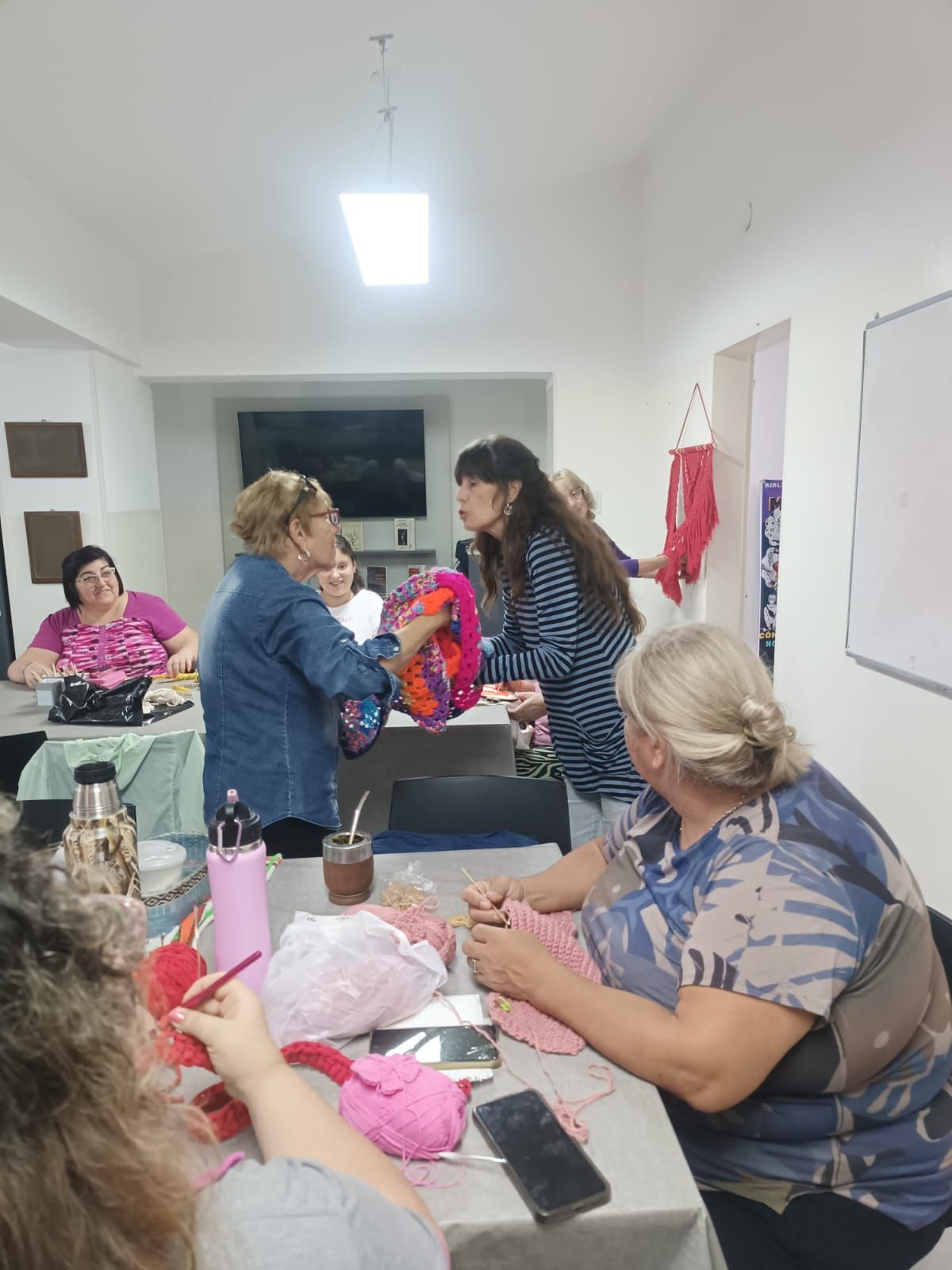 En una habitación luminosa, la gente se reunió alrededor de una mesa, charlando y manipulando objetos coloridos.