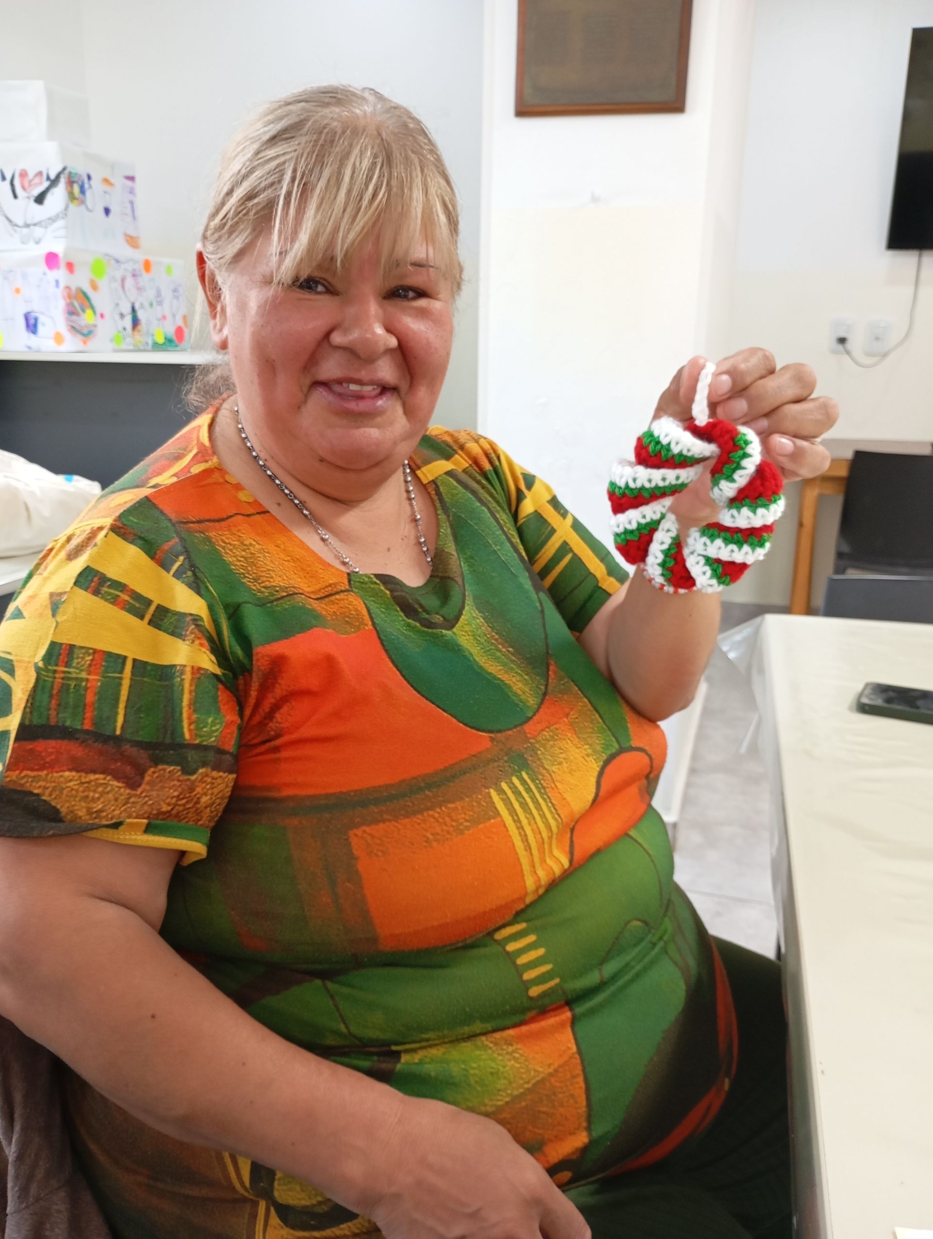 Mujer sonriendo y sosteniendo un adorno navideño rojo y verde en una habitación luminosa.