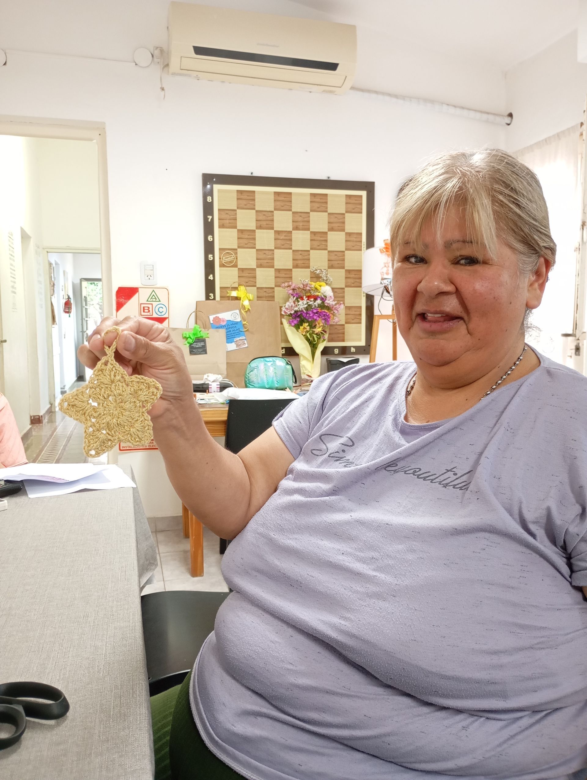 Mujer sonriente con una camisa lila sosteniendo una bolsa de palomitas de maíz en una acogedora habitación