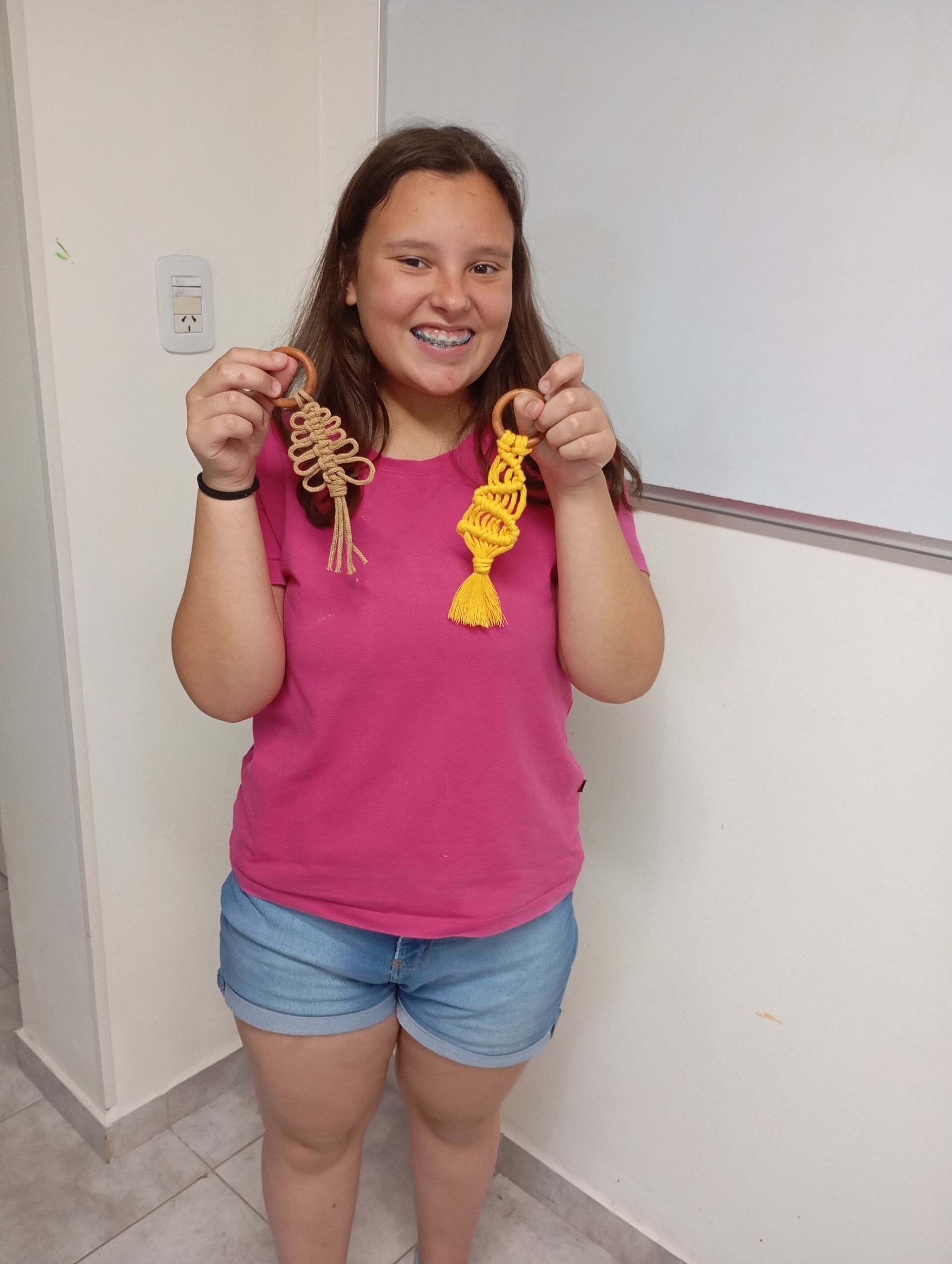 Mujer con camisa rosa y pantalones cortos vaqueros sonriendo y sosteniendo dos cintas trenzadas
