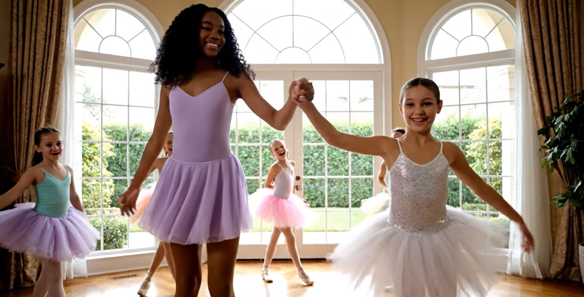 Ballet instructor and students in a dance studio, holding hands while smiling, sunlight.