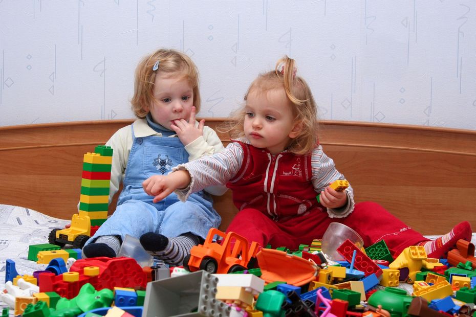 Dos niños pequeños sentados entre coloridos bloques de construcción, mirando juguetes en el suelo.