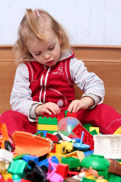 Niño con un atuendo rojo jugando con juguetes coloridos en el suelo dentro de casa.