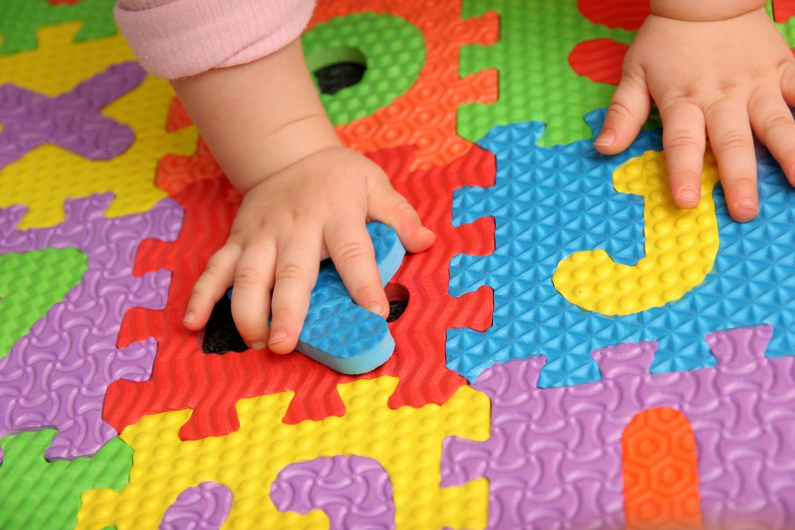 Las manos de un niño sobre una colorida alfombra de espuma para rompecabezas