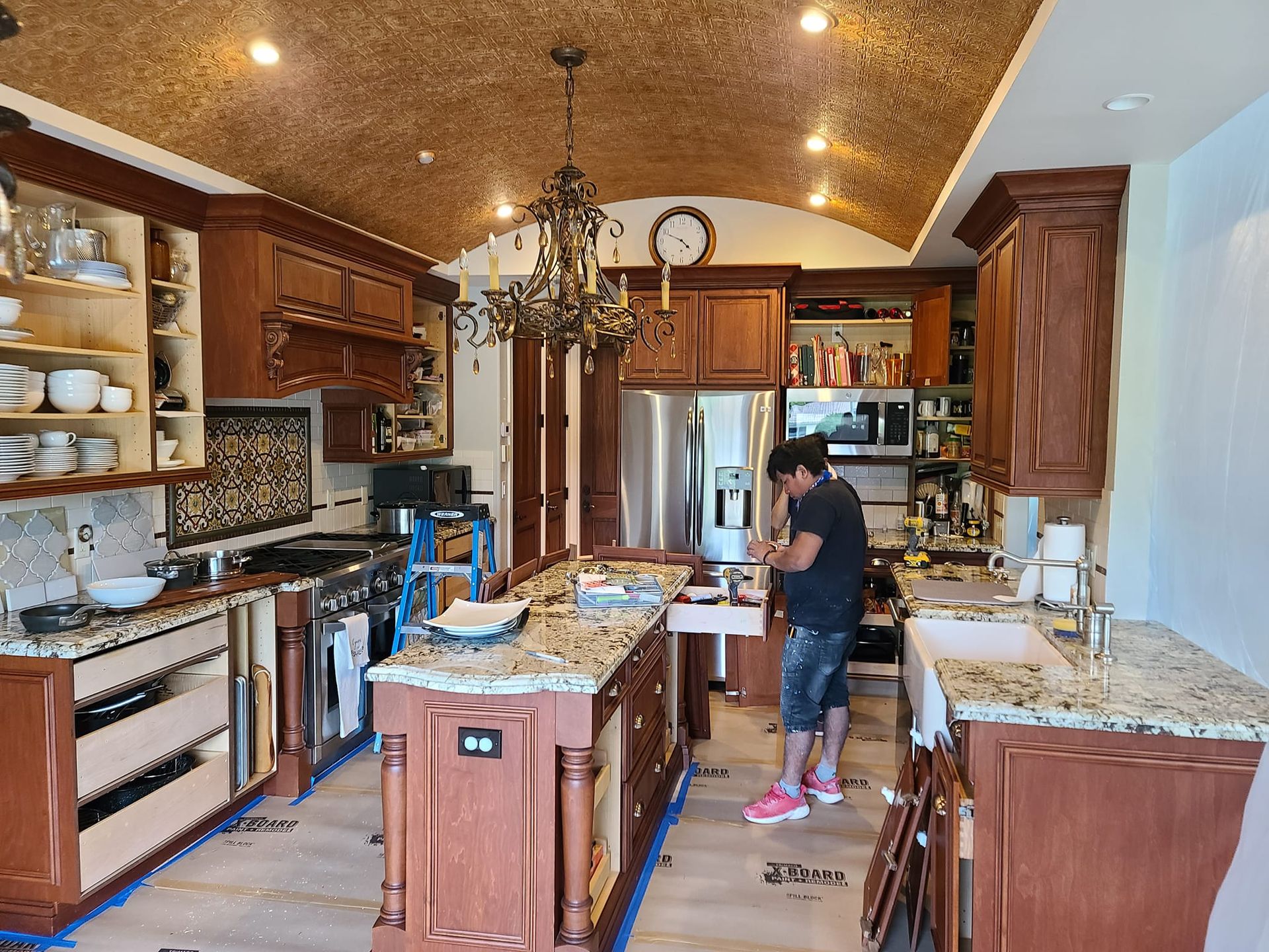 Kitchen with wooden cabinets, granite countertops, a person working, and decorative ceiling.