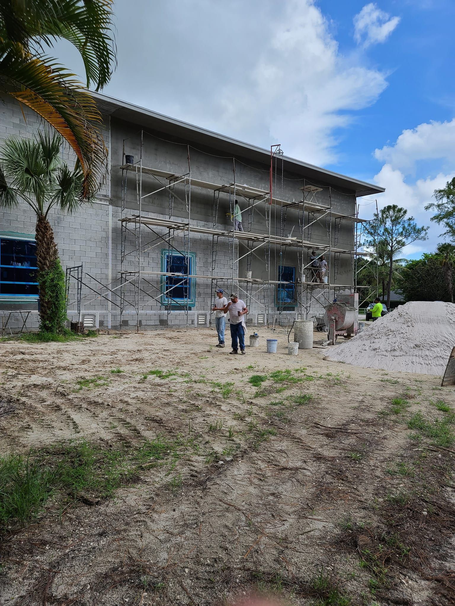 Construction site with scaffolding on a two-story building, workers, and materials under a blue sky.