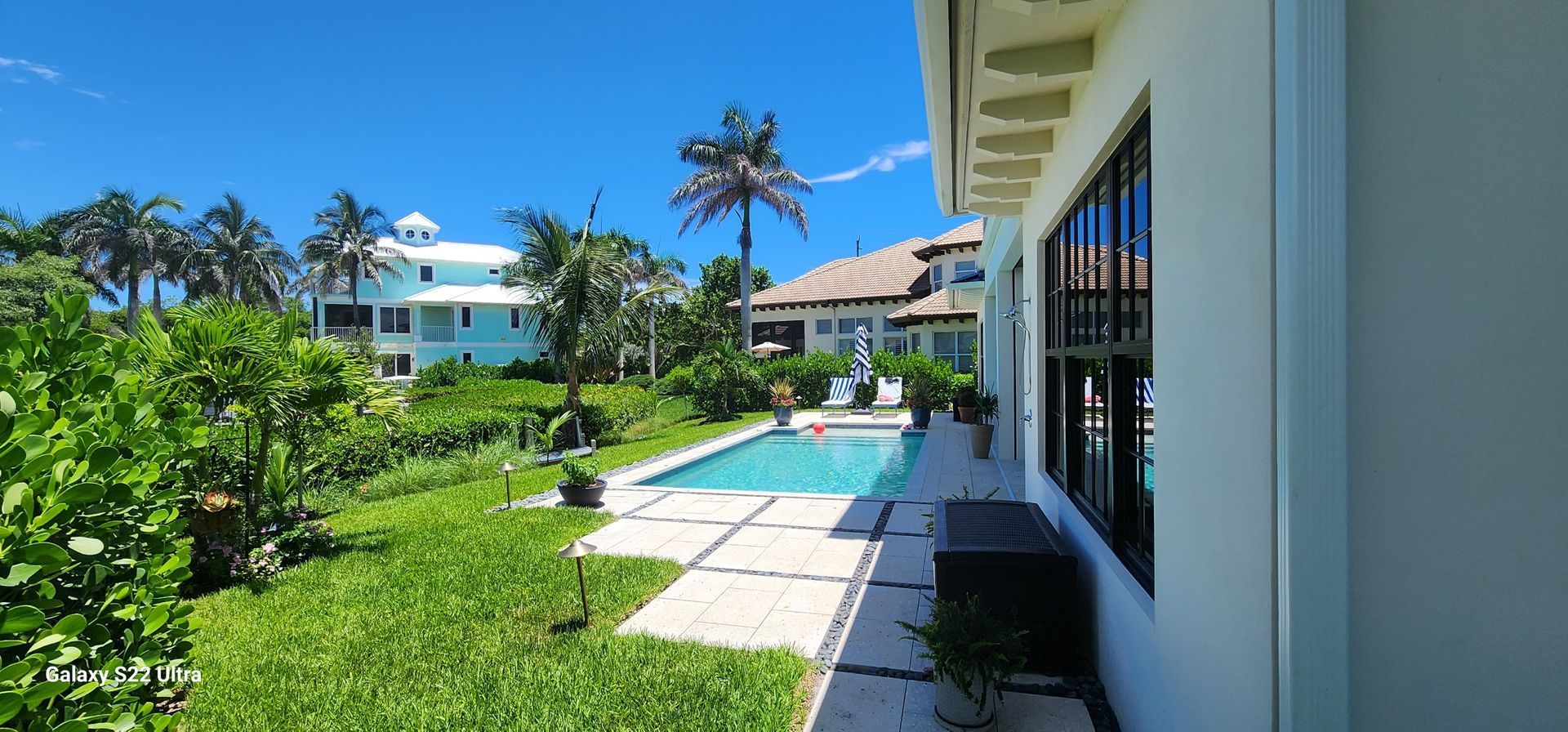 Exterior of a home with a swimming pool and tropical landscaping on a sunny day.
