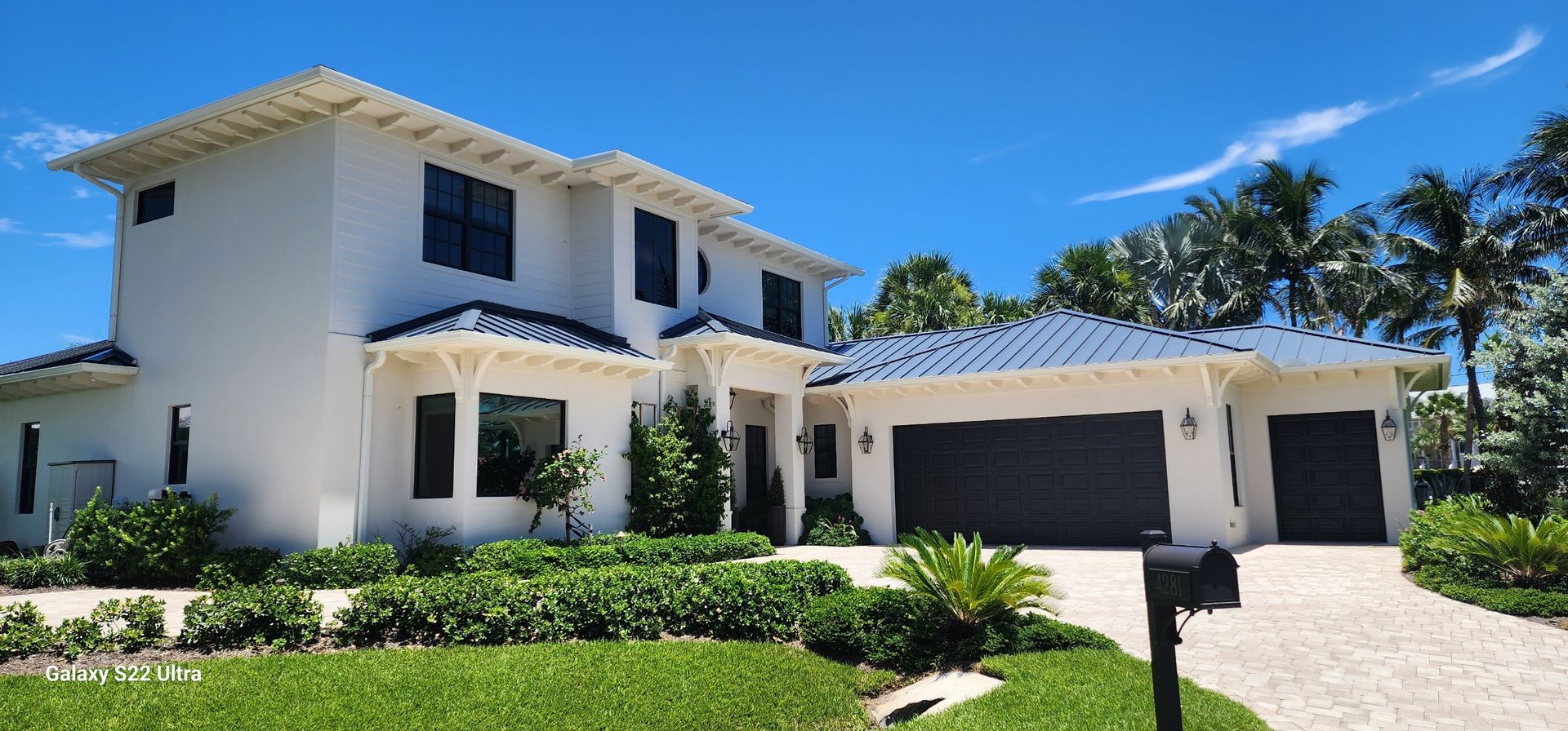 White stucco house with dark roof and trim, green landscaping, blue sky.