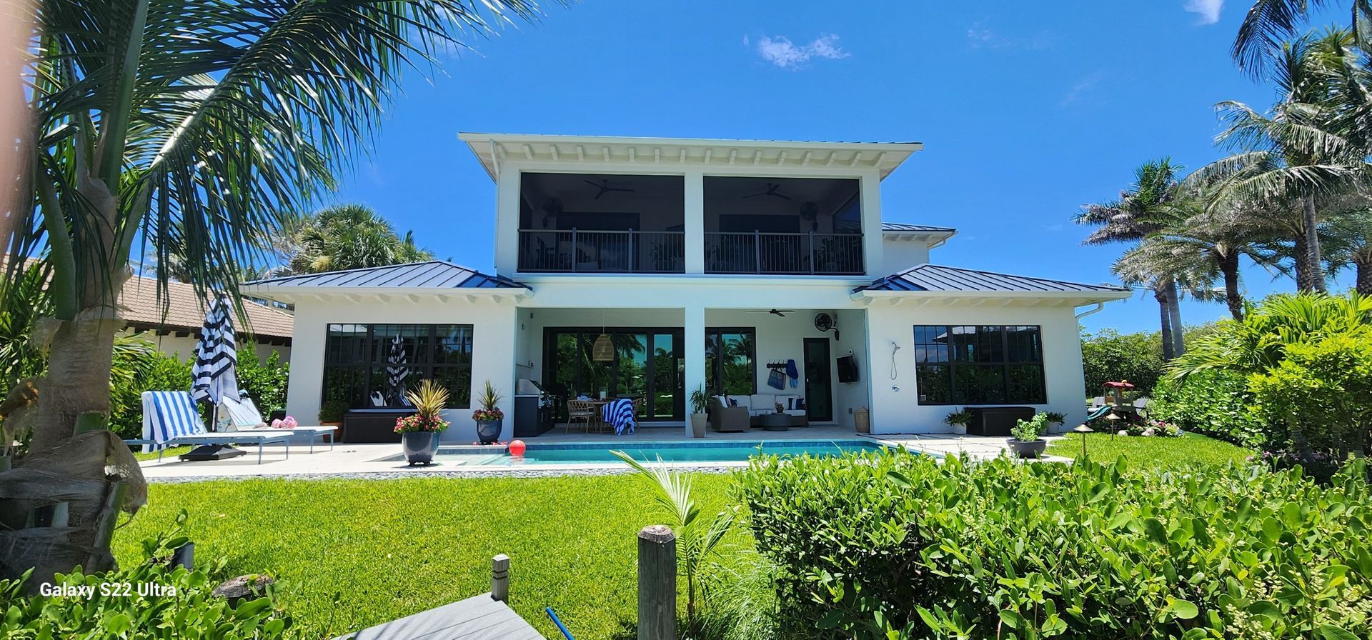 Back of a white two-story house with a pool and lush green lawn under a blue sky.