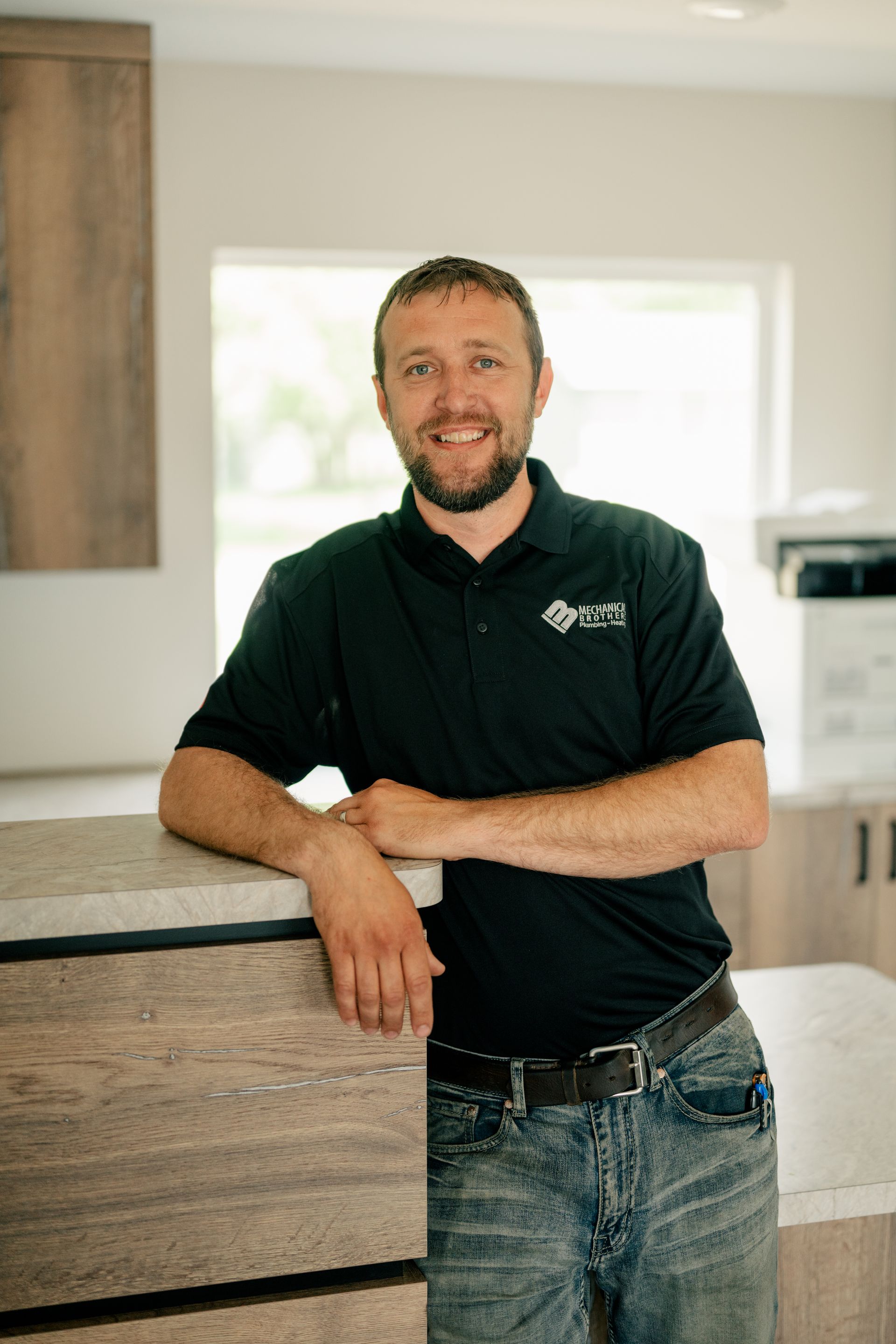 A man with a beard is leaning on a counter in a kitchen.