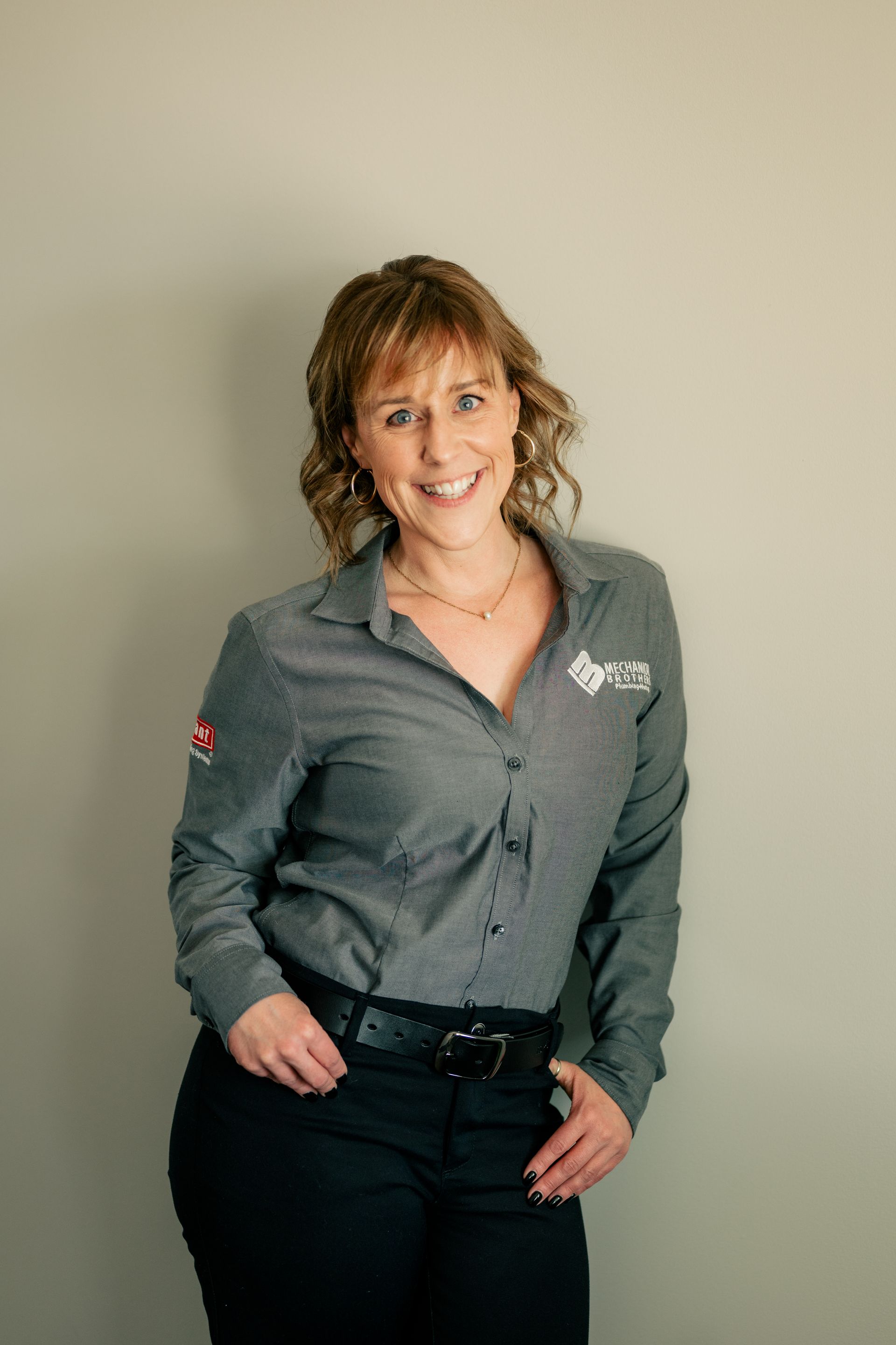 A woman in a grey shirt and black pants is standing in front of a wall.