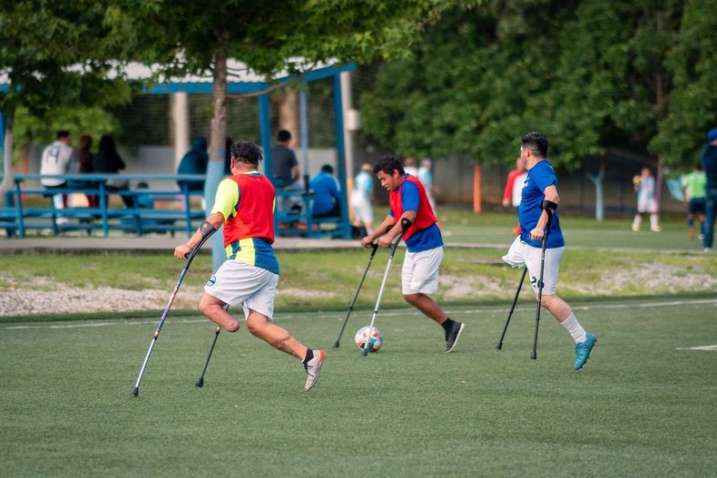 Three people playing soccer on crutches on a grassy field
