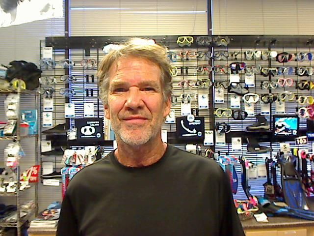 Man in black shirt stands in front of swimming gear display.