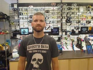 Man in a gray shirt with a skull graphic stands in a store with scuba gear displays.