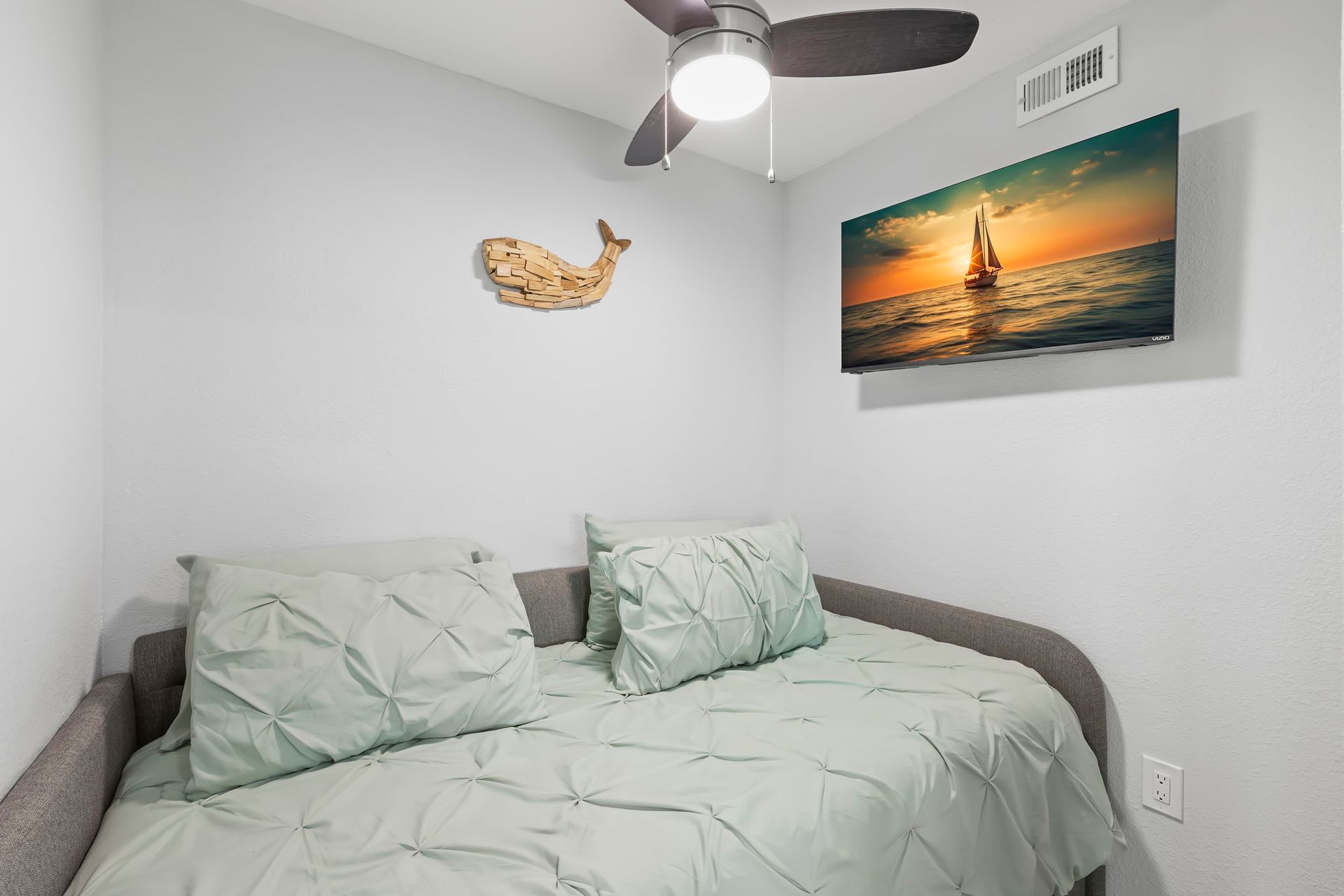 A bedroom with a bed , ceiling fan , television and a painting of a seahorse on the wall.