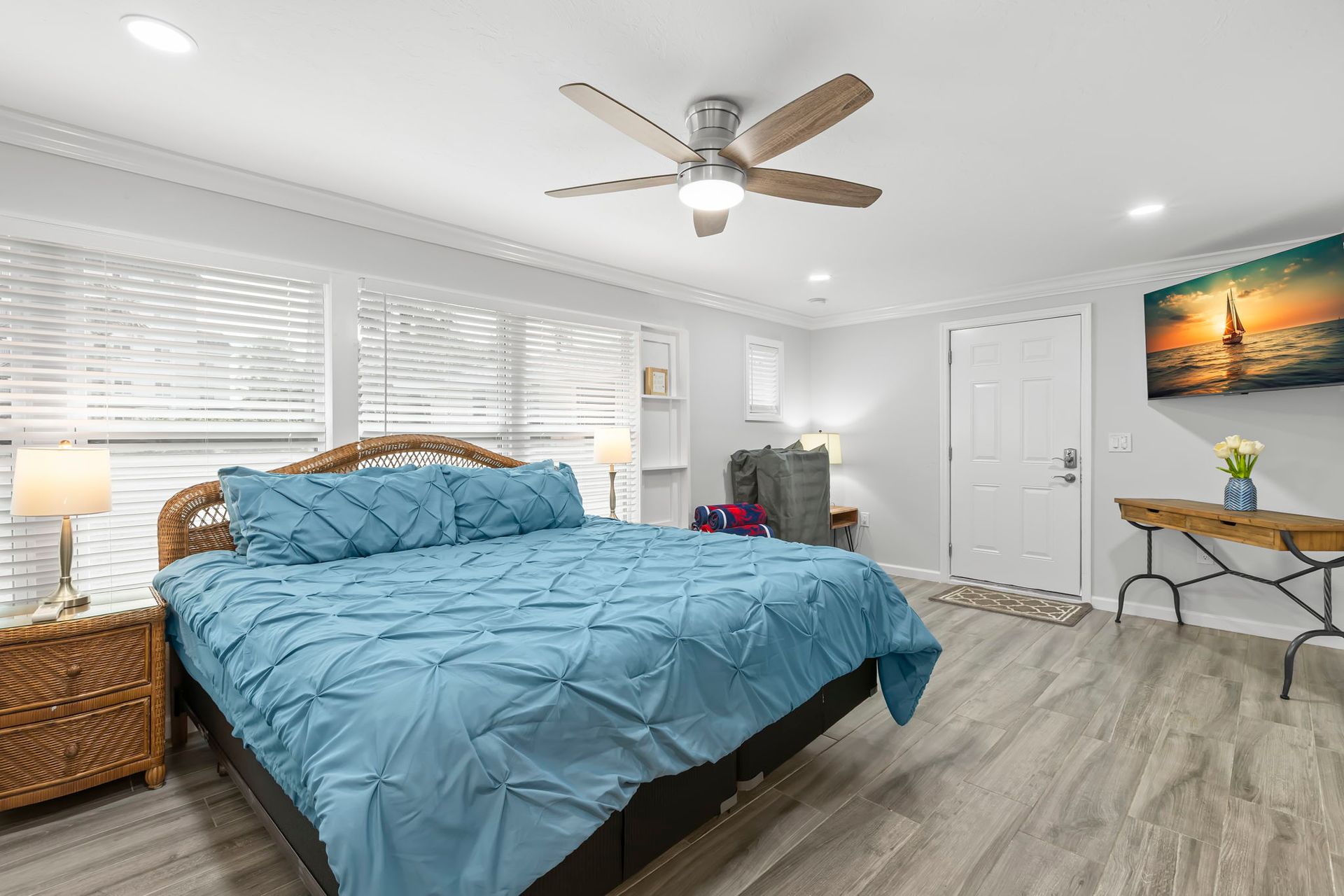 A bedroom with a bed , ceiling fan , television and sliding glass doors.