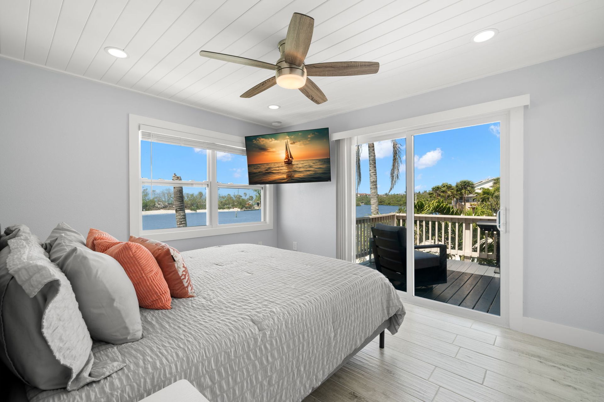 A bedroom with a bed , ceiling fan , television and sliding glass doors.