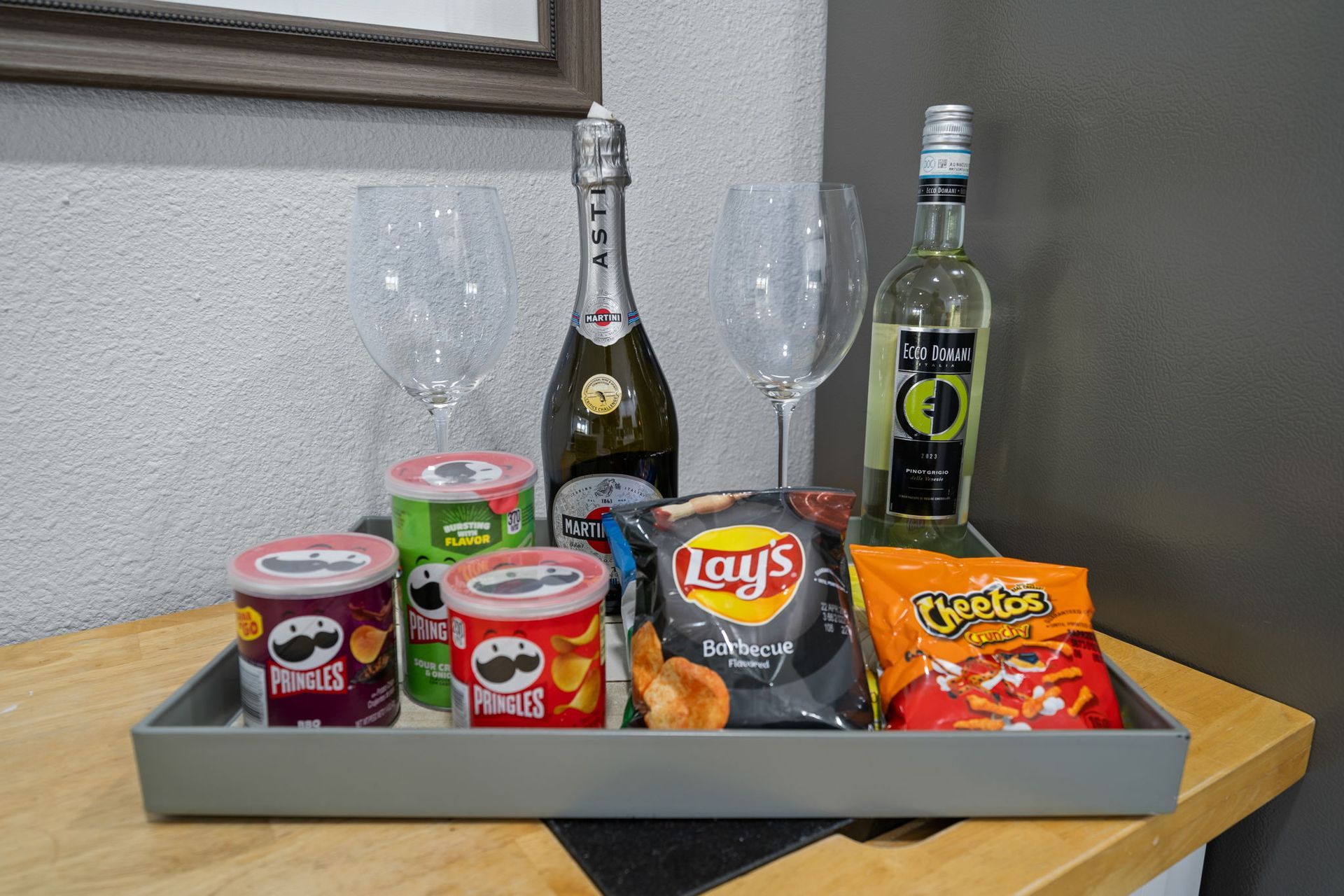 A tray with a bottle of wine , chips , and glasses on a table.