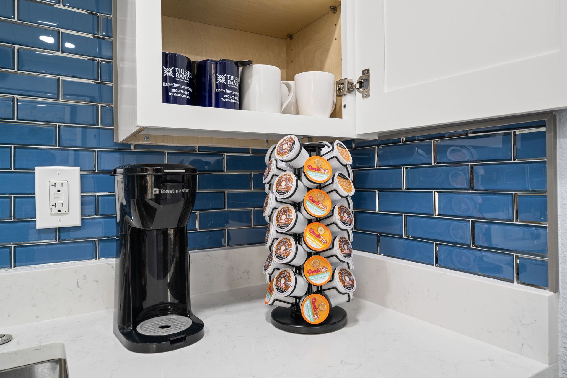 A kitchen with blue tiles , a coffee maker , and a k cup holder.