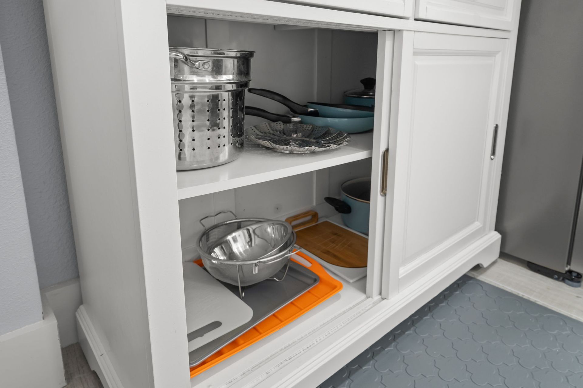 A white cabinet with a cutting board and pots and pans in it.