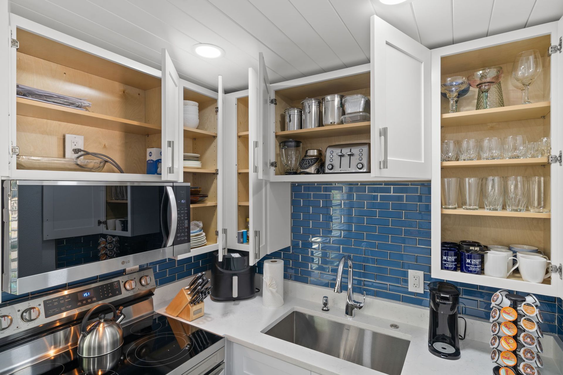 A kitchen with a sink , stove , microwave , and shelves.