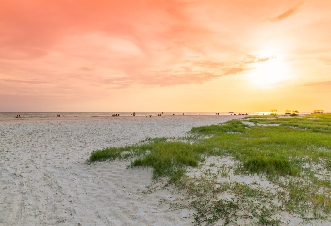 A sunset over a sandy beach with people walking on the beach.