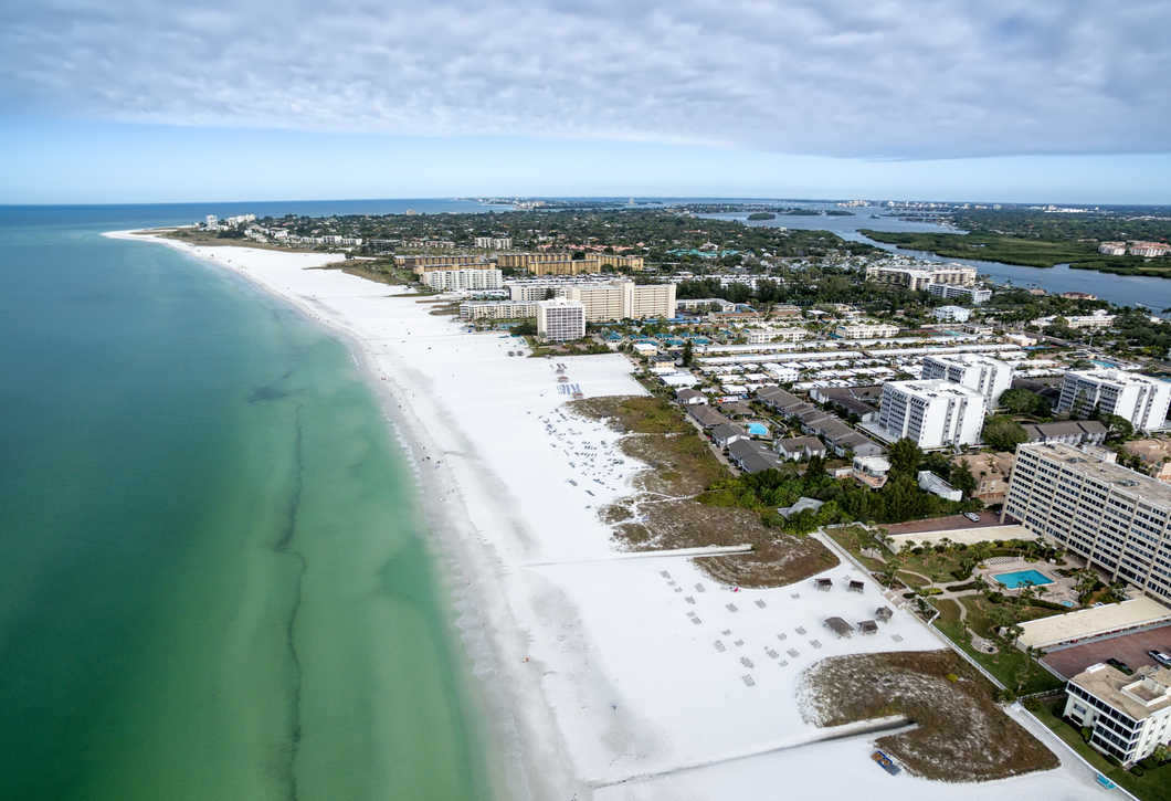 An aerial view of a beach with white sand and buildings in the background.