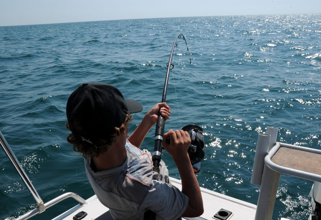 A man is fishing on a boat in the ocean.