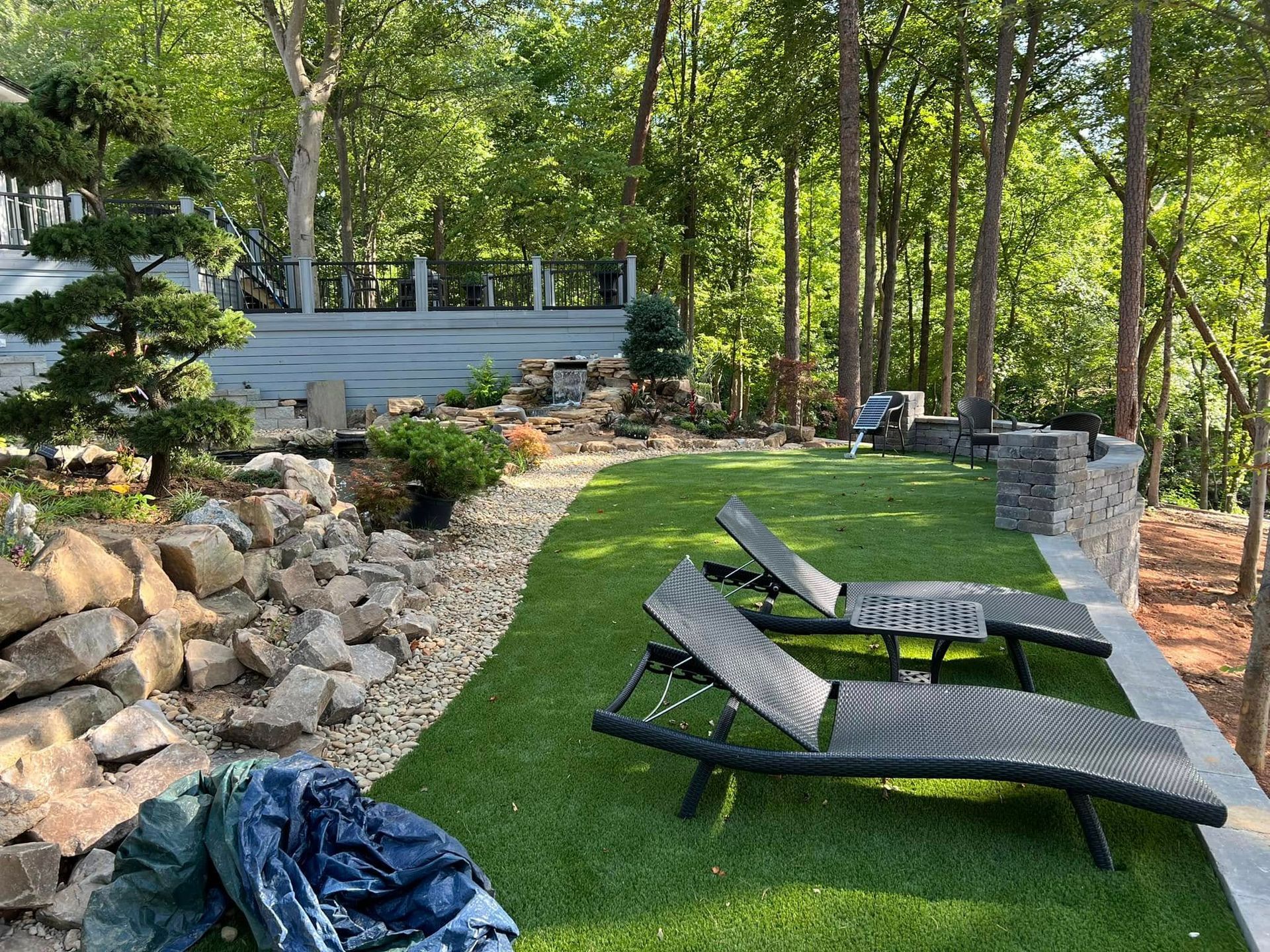 Backyard patio with lounge chairs, stone landscaping, and a wooded garden backdrop