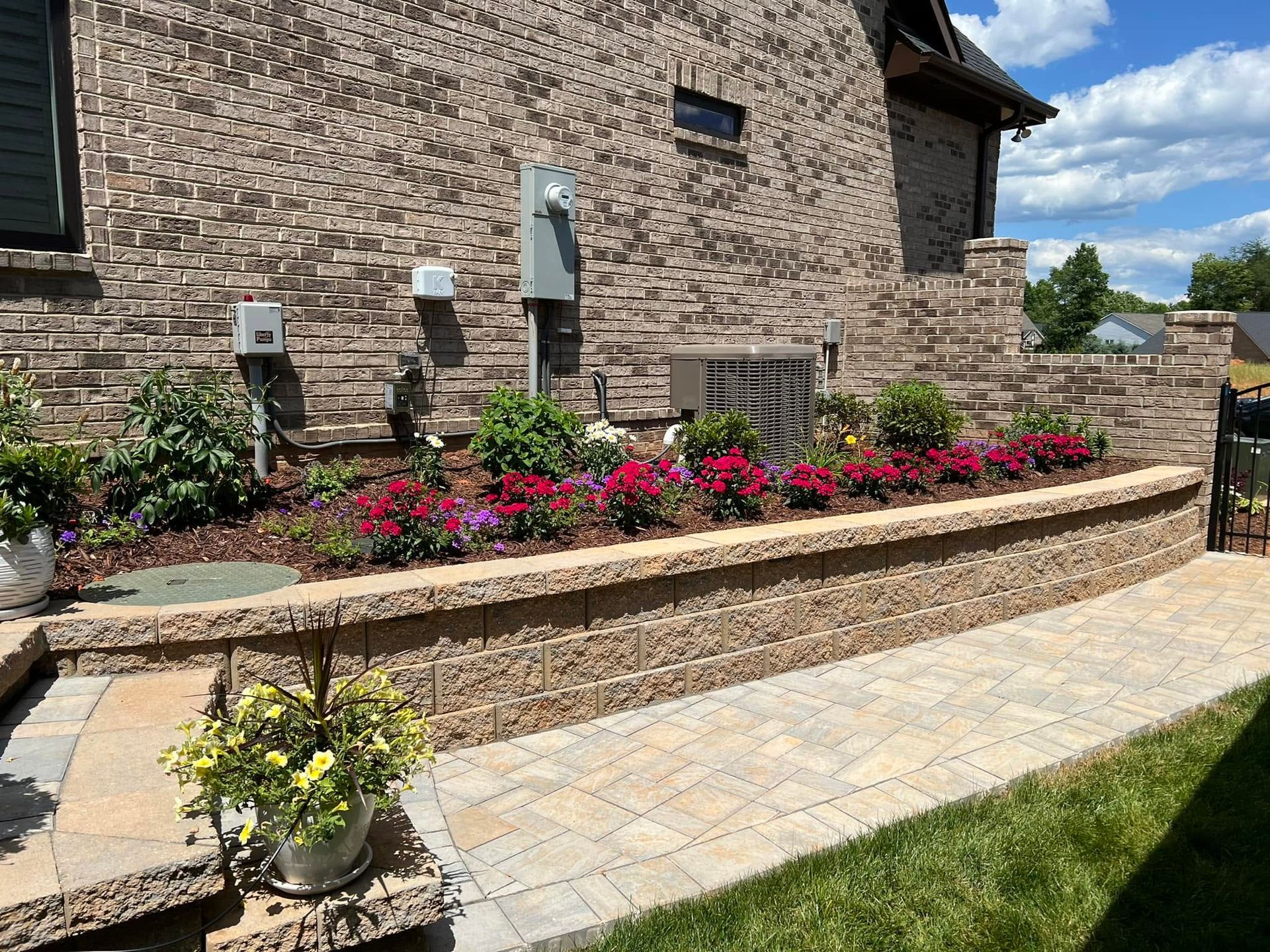 Stone house exterior with raised flower beds and a curved brick retaining wall beside a paved walkway