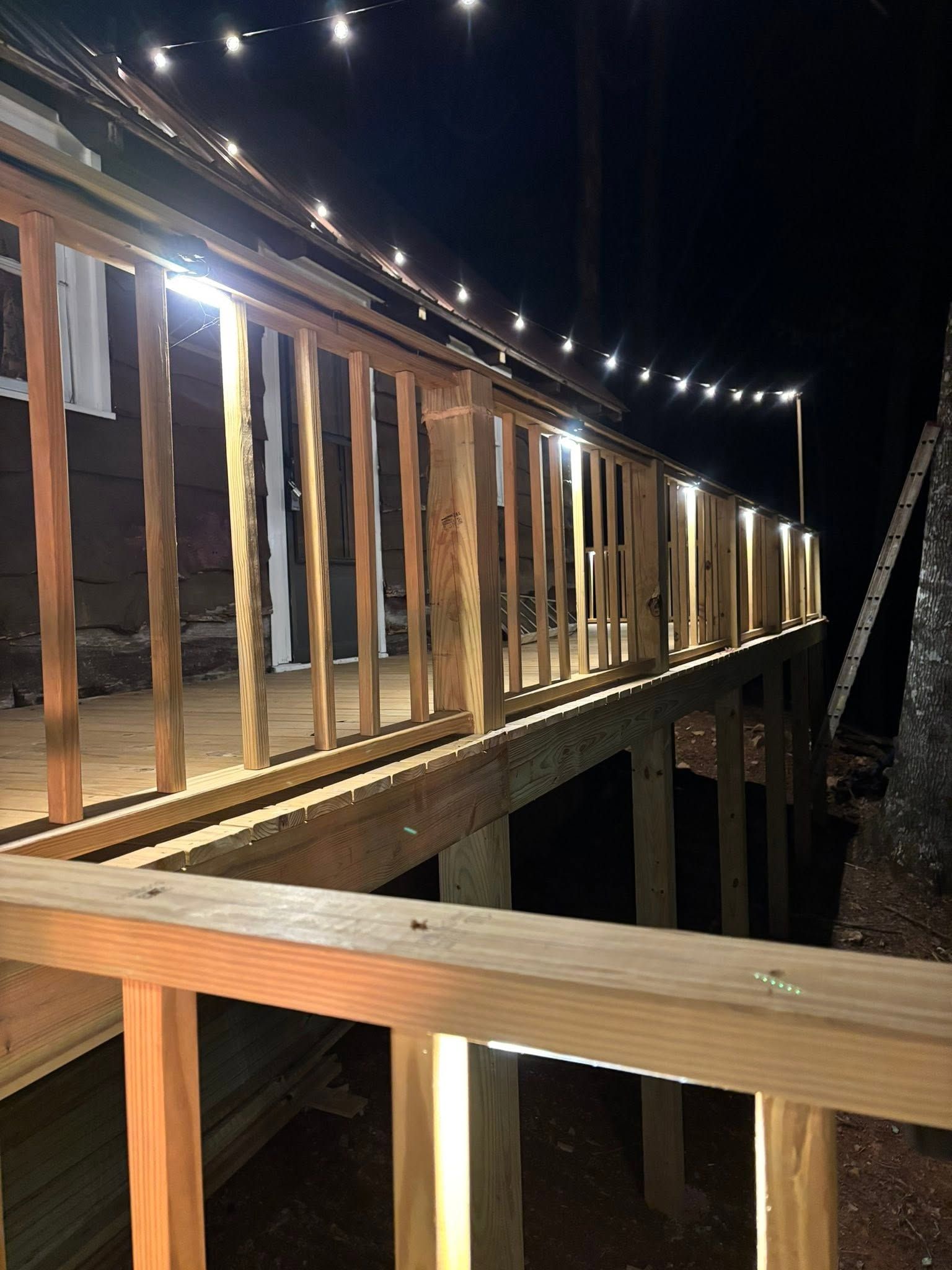 Wooden boardwalk lit by string lights at night, with railings and steps leading into darkness