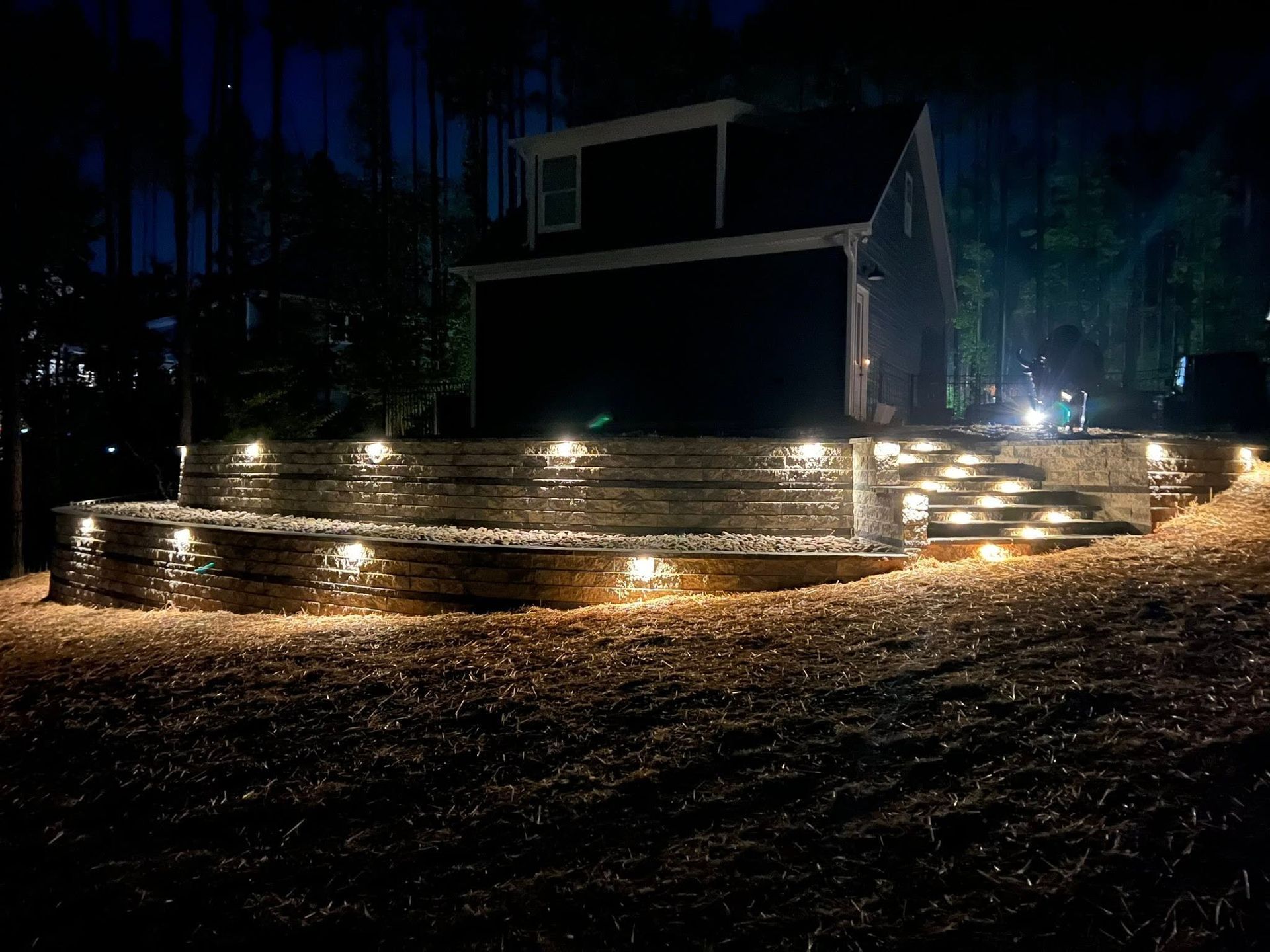 Nighttime deck with warm lights in front of a dark house in a wooded area