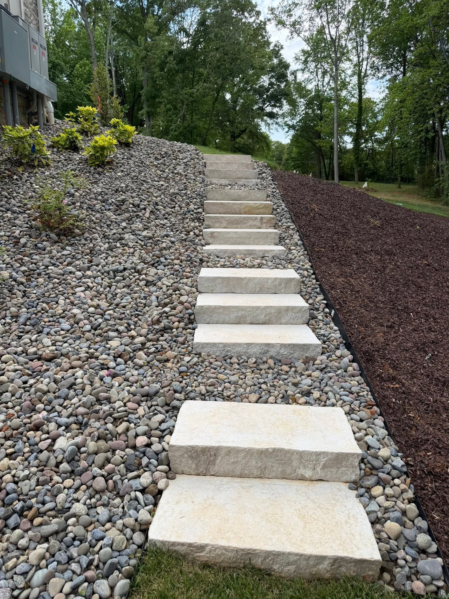 Stone steps ascending a landscaped hillside with gravel, dark mulch, and trees.