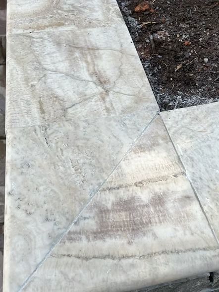 Close-up of a cracked concrete sidewalk with a triangular patch and dirt along the edge