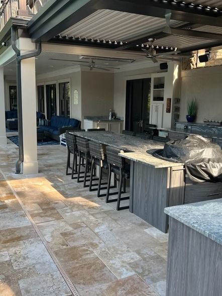 Covered outdoor patio with bar seating, stone floor, and modern kitchen setup in a backyard.