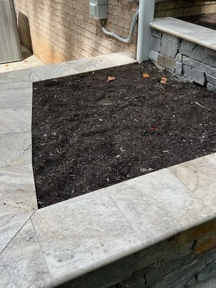 Empty garden bed bordered by stone pavers beside a brick wall and steps