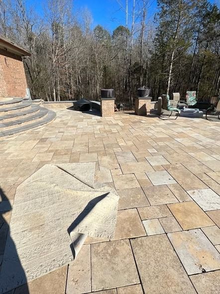 Stone patio with steps, outdoor seating, and a wooded backyard under a clear blue sky