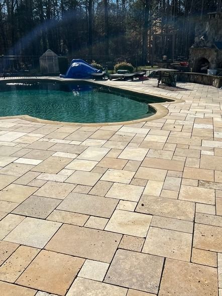 Backyard pool with stone patio and lounge chairs in bright sunlight