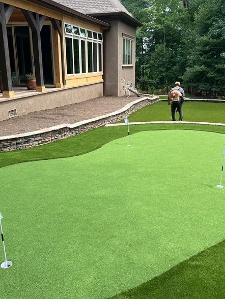 Backyard putting green beside a house, with a person standing near the far edge