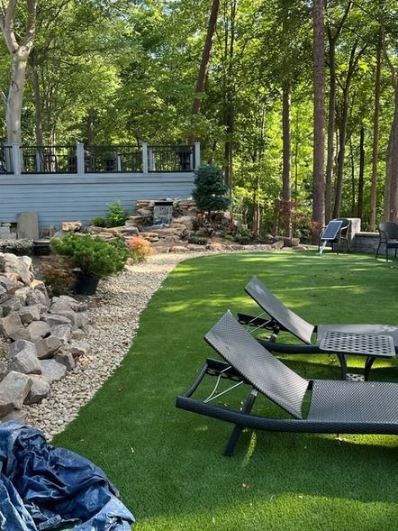 Lounge chairs on a green lawn beside a rock garden and trees in a backyard