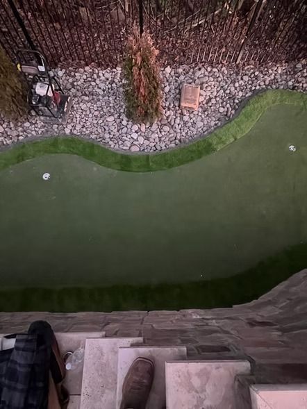 Overhead view of a miniature golf green with two white balls and stone-edged landscaping.