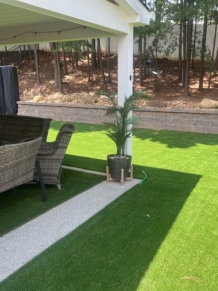 Covered patio with wicker chair, potted palm, and green lawn in bright sunlight