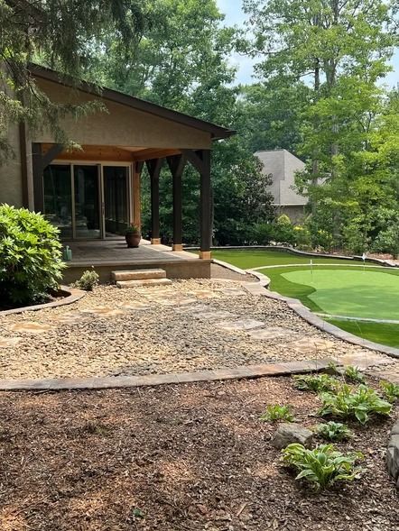 Wooded backyard patio with stone steps, green lawn, and a covered porch with columns