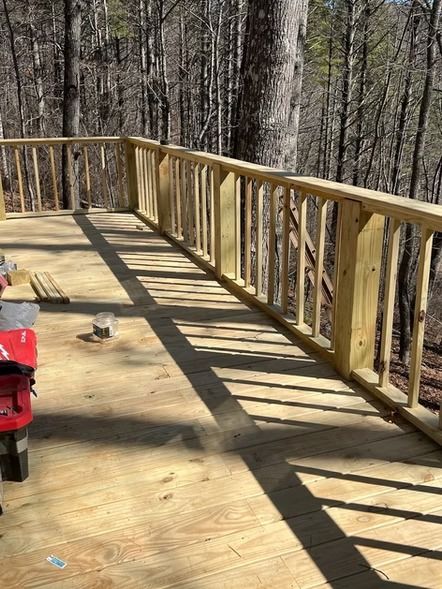 Wooden deck with railing in a wooded area, with a red chair and a small object on the floor.