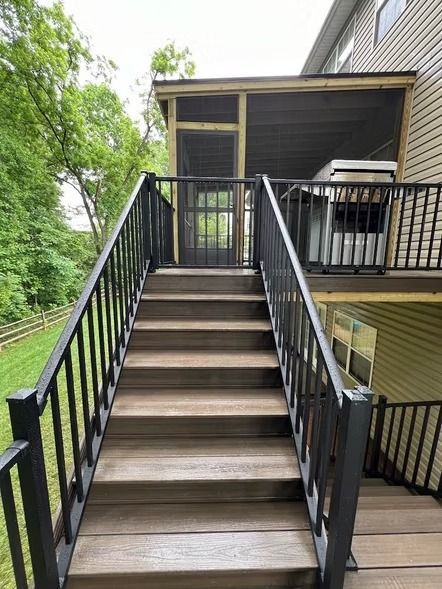 Exterior staircase with black railings leading to an elevated wooden deck beside a house